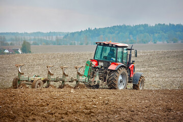 Tractor cultivating field. Tractor plowing soil on farm field. Tractor harrow plowing soil, rural landscape background. Soil cultivation, farm life. Сountryside landscape.