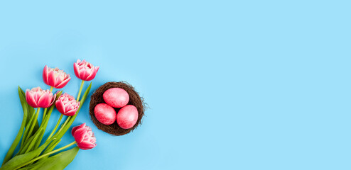Happy Easter greeting card, banner. Pink easter eggs in a nest and a bouquet of tulips on a blue background. Copy space. Top view. 
