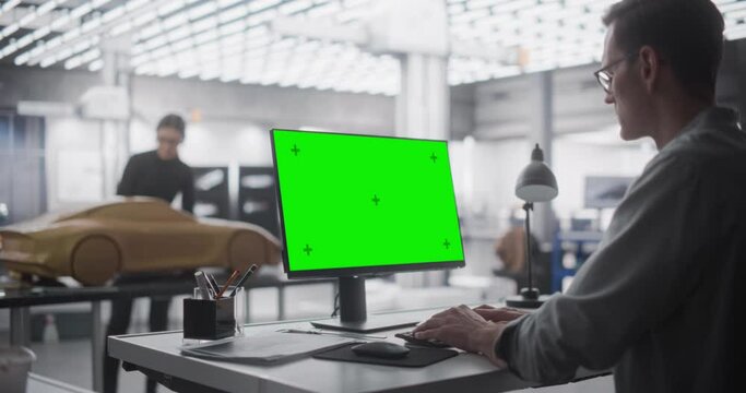 Automotive Designer Working on a Desktop Computer with Green Screen Mock Up Display. Digital Artist Creating a Concept Vehicle in a Studio. Modeler Working on Clay Model in the Background