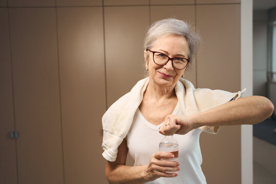 Gray-haired grandmother in glasses opens a bottle of water
