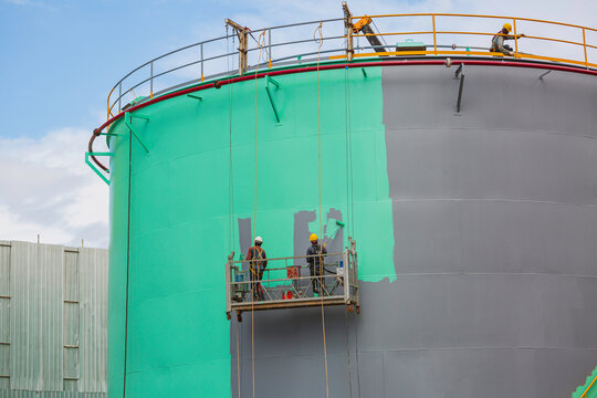 The male worker takes the cable car holding an industrial painting brush used for shell plate tank oil surface surface green color