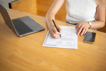 Close-up shot of beautiful young woman working with laptop and phone with documents on table at home
