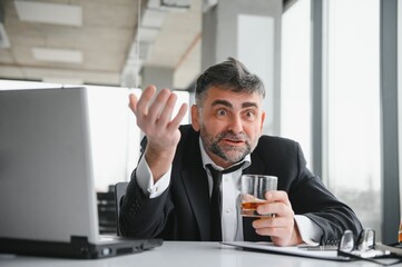 Old male employee drinking alcohol at workplace