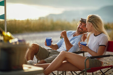 young adult couple talking and smiling, looking each other, sitting outdoor at sunset