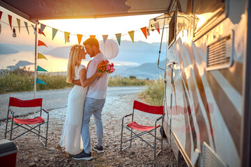 young adult couple hugging, holding each other in arms,   in love, in front of a camper outdoor at...