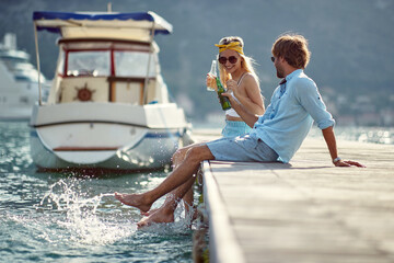 adult caucasian couple sitting on a dock, talking, smiling, laughing, splashing water with legs, having fun at the seaside.