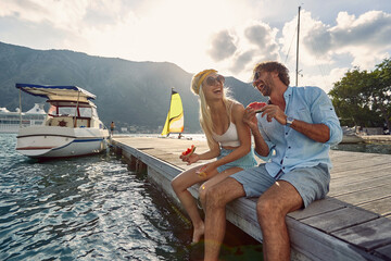 young adult couple sitting at the dock, eating watermelon, laughing, looking each other