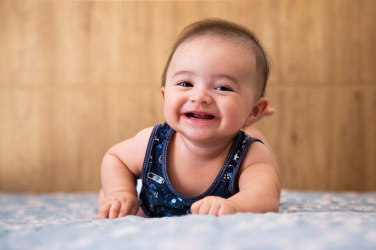 baby lying on a bed, looking forward and smiling.