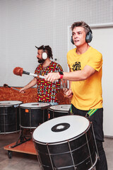 Two boys play drums energetically inside a studio with ear protections