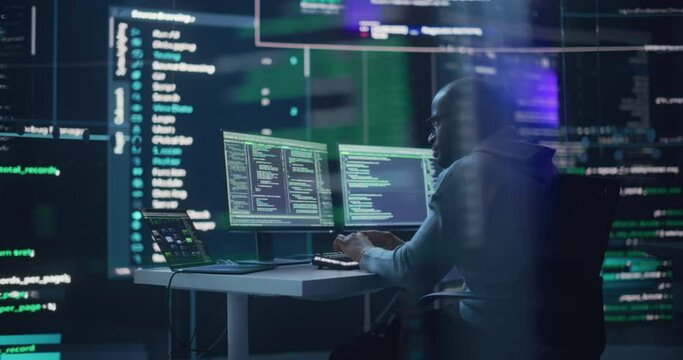 Portrait of a Black Man Working on Computer, Typing Lines of Code that Appear on Big Screens Surrounding him in Monitoring Room. Male Programmer Creating Innovative Software Using AI Data and System