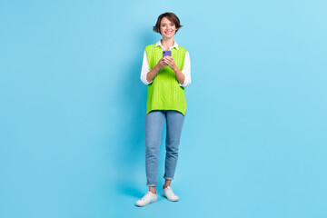 Fototapeta na wymiar Full length photo of good mood woman with bob hairstyle dressed green waistcoat holding smartphone isolated on blue color background