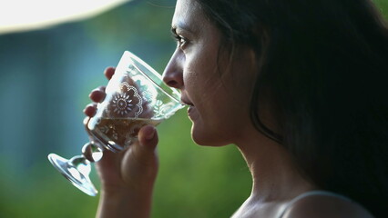 Woman drinks white wine outdoors. Closeup of female person holding glass of alcoholic beverage while staring at view