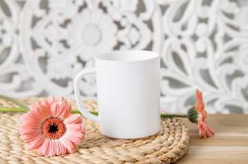 Selective focus on single one white mug mock up. Cup on home table with decorative spring flowers on background and bohemian style wood panel. Cozy seasonal products advertisement background.