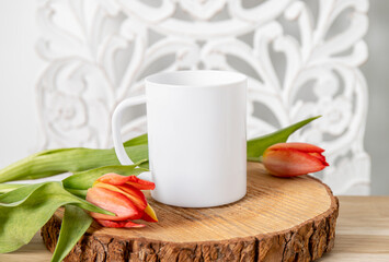 Selective focus on single one white mug mock up. Cup on home table with decorative spring flowers on background and bohemian style wood panel. Cozy seasonal products advertisement background.