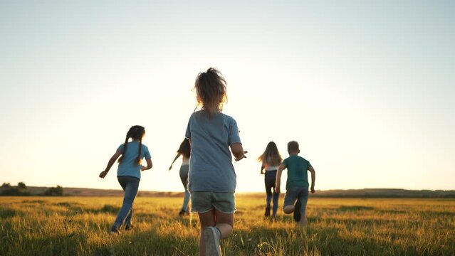 Happy family of children in summer outdoors.Children run together on grass in meadow.Silhouette of group of people playing in field.Boys and girls have fun run in the park at sunset.The Joy of Friends