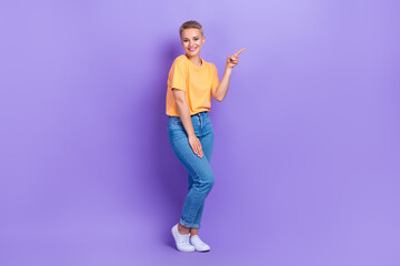 Full length photo of friendly cheerful cute girl dressed jeans white sneakers directing empty space isolated on violet color background