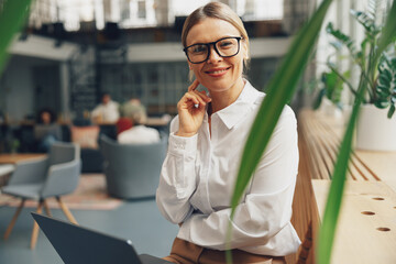 Smiling stylish woman office worker looking at camera while working on laptop in office near window