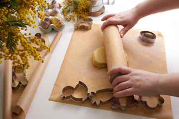 Female hands roll out the dough for Easter cookies over the table in spring decor