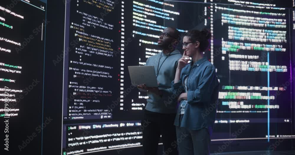 Leinwandbilder Portrait Two Diverse Developpers Using Laptop Computer, Discussing Lines of Code that Appear on Big Screens Surrounding Them. Male and Female Programmers Creating a Software Together, Fixing Bugs