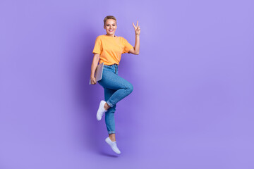 Fototapeta na wymiar Full body portrait of attractive energetic lady jumping hold netbook show v-sign isolated on purple color background