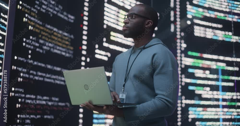 Poster Portrait of Young Black Man Working on Laptop Computer, Looking at Big Digital Screen Displaying Back-end Code Lines. Professional Programmer Developing a Big Data Interface Software Project