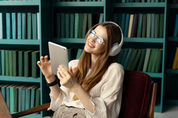 A cheerful female student listens to music and audiobooks in the app, using headphones on her head.