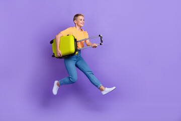 Full length photo of cheerful gorgeous girl dressed jeans white sneakers hold bag look empty space isolated on violet color background