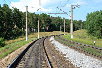 A railway with a line of electric columns and trees along in the background