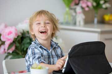 Little toddler child, blond boy, licking lollipop while watching movie on tablet - obrazy, fototapety, plakaty