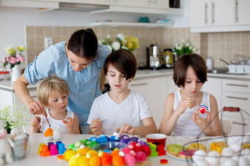 Three children, sibling brothers, painting easter eggs for decoration, mom helping them