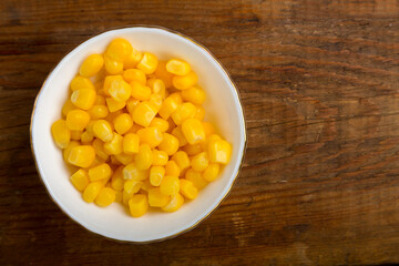 Corn grains in a white plate on a wooden table. save a place.