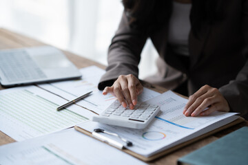 Close up view of businesswoman using calculator while analyzing the business chart in the office room.