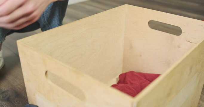 Women's hands put different clothes in box. Side view, indoors. Concept of collecting things for donations, throw away, charity, clean up, housework, storage.