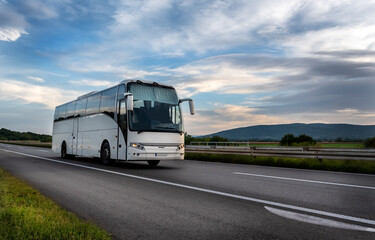 Fototapeta na wymiar White Modern comfortable tourist bus driving through highway at bright sunny sunset. Travel and coach tourism concept. Trip and journey by vehicle