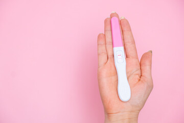 Female hand holding a positive pregnancy test on the pink background. Planning of pregnancy and...