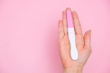 Female hand holding a positive pregnancy test on the pink background. Planning of pregnancy and motherhood concept with copy space 