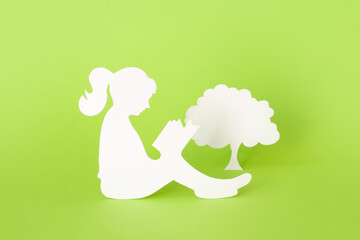 Paper silhouette of a girl reading a book and tree isolated on green background