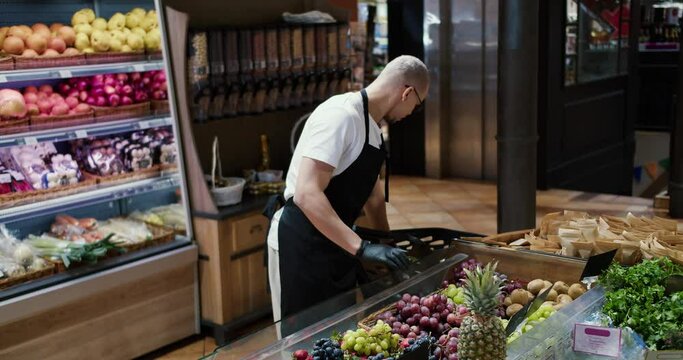 Man worker in black apron and gloves stocking the fruits in supermarket