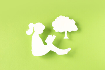 Paper silhouette of a girl reading a book isolated on green background
