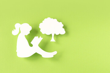 Paper silhouette of a girl reading a book isolated on green background