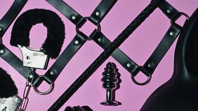 Handcuffs, whip flogger for BDSM sex with submission and domination. A set of adult intimate erotic sex toys on a pink background