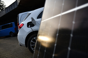 Elektroauto, das vor einem Solarpanel aufgeladen wird. Sonne spiegelt sich im Photovoltaik Modul....