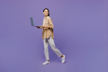 Full body side view young IT latin woman wear light shirt casual clothes hold use work on laptop pc computer look aside on area go isolated on plain pastel purple color background. Lifestyle concept.