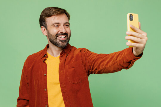 Elderly man 40s years old he wears casual clothes red shirt t-shirt doing selfie shot on mobile cell phone post photo on social network isolated on plain pastel light green background studio portrait.