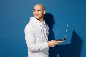 Side view young smiling IT man of African American ethnicity wear white hoody hold use work on...