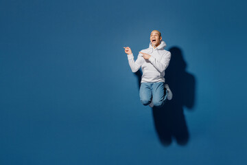 Full body young fun happy man of African American ethnicity wearing white hoody jump high point index finger aside on workspace area isolated on plain dark royal navy blue background studio portrait.