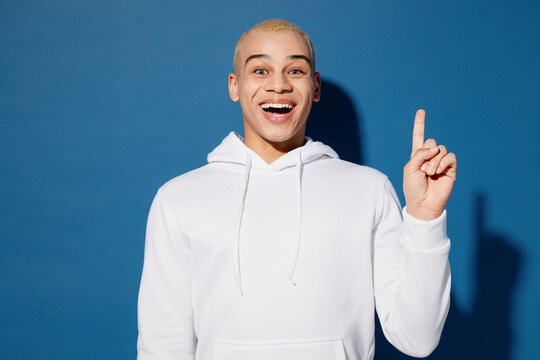 Young insighted smart proactive fun dyed blond man of African American ethnicity wear white hoody holding index finger up with great new idea isolated on plain dark royal navy blue background studio.