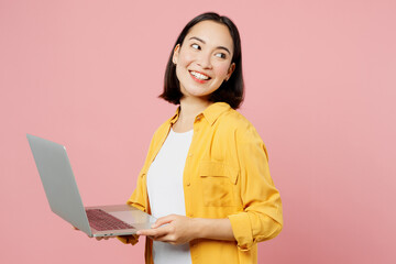 Young IT woman of Asian ethnicity wears yellow shirt white t-shirt hold use work on laptop pc...