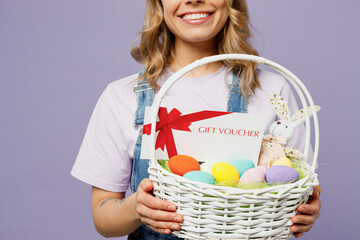 Cropped young woman wearing casual clothes bunny rabbit ears hold wicker basket colorful eggs gift certificate coupon voucher card for store isolated on plain purple background Happy Easter concept.