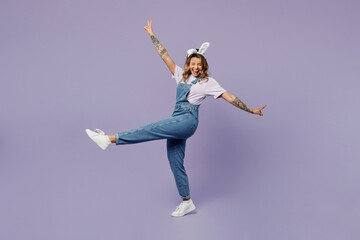Full body side view young woman wear white casual clothes bunny rabbit ears stand with outstretched hands raise up leg isolated on plain pastel light purple background. Lifestyle Happy Easter concept.